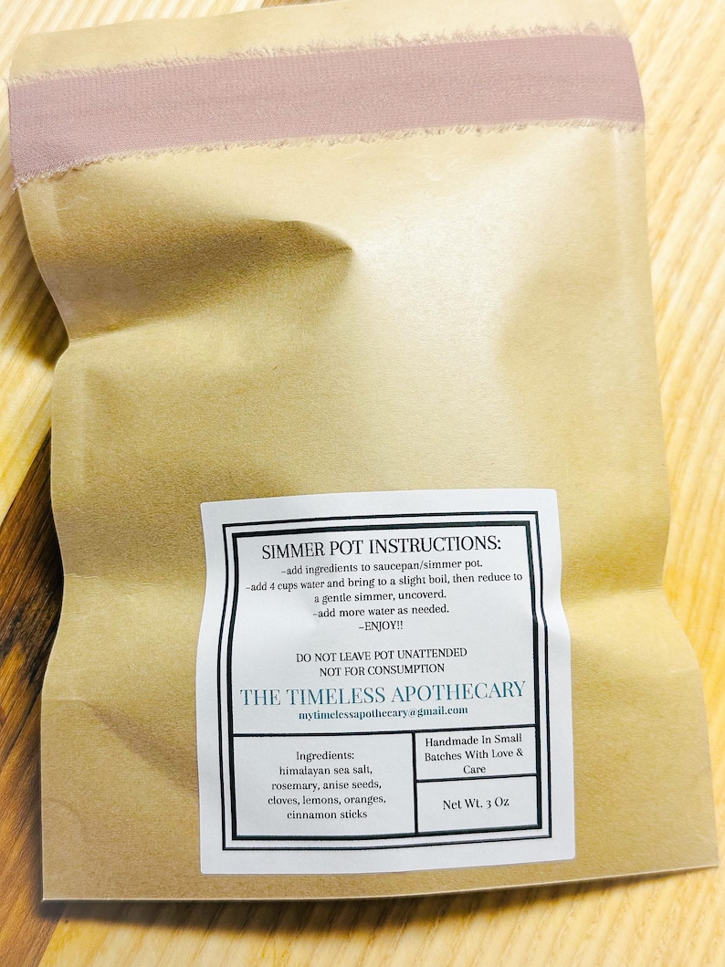 May include: A brown paper bag with a label that reads "Simmer Pot Instructions." The label lists ingredients like Himalayan sea salt, rosemary, and cinnamon sticks. The bag is sealed with a pink ribbon. Net weight is 3 oz.