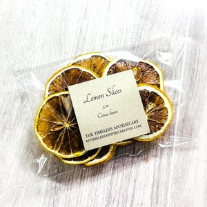 May include: A clear plastic bag containing dried lemon slices. The slices are yellow and brown, with a label that reads "Lemon Slices" and "Citrus limon". The product is from The Timeless Apothecary.