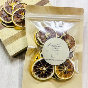 May include: Dried lemon slices in a clear plastic bag with a brown paper backing. A round label reads "Lemon Slices Citrus limon" and "The Timeless Apothecary". Several lemon slices are on a wooden cutting board.