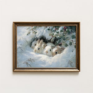 May include: A framed painting shows four rabbits in a snowy setting. The rabbits, white and brown, are partially hidden in the snow, with green foliage and red berries above. The frame is a warm gold colour.