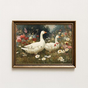 May include: A framed wall art print featuring an oil painting of two white geese standing in a vibrant meadow filled with red, pink, yellow, and white wildflowers. The artwork is enclosed in a dark brown wooden frame with a simple, classic profile.