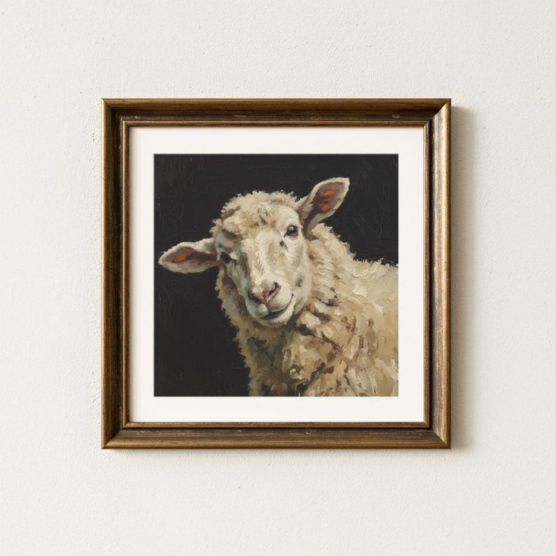 Op de afbeelding: Een ingelijst schilderij van een schaap met een lichtgekleurde wollen vacht en een roze neus en oren. Het schaap staat tegen een zwarte achtergrond. De lijst heeft een donkerbruine, warme kleur.