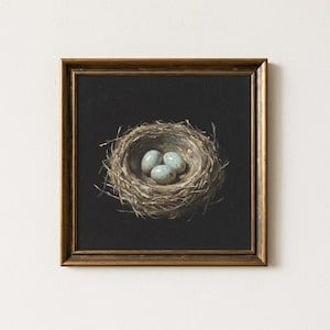 May include: A framed painting of a bird's nest with three speckled blue eggs. The nest is made of twigs and sits against a black background. The frame is a dark, warm brown color.