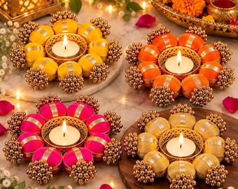 May include: Four circular candle holders arranged in a group, each featuring a central tea light surrounded by eight fabric-wrapped spheres in yellow, orange, pink, and gold, accented with clusters of small metallic gold beads.