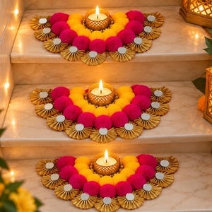 Puede incluir: Tres decoraciones semicirculares con pompones de color amarillo brillante y rosa intenso dispuestos en arcos. Cada pieza incluye abanicos de tela dorada plisada con pequeños espejos circulares y una vela de té encendida.