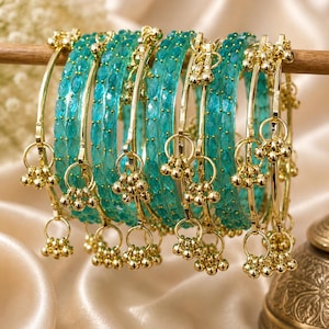 May include: A set of turquoise bangles featuring a faceted, translucent texture. Each bangle is accented with gold-toned metal rings and small, dangling gold-toned spherical charms that hang from the circular frame of the jewelry pieces.