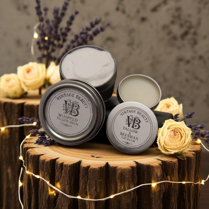 Puede incluir: Una disposici&oacute;n de productos de b&aacute;lsamo de sebo Vintage Beauty. La imagen muestra varias latas peque&ntilde;as, redondas y plateadas con etiquetas blancas y texto negro. Las latas est&aacute;n dispuestas sobre una superficie de madera, rodeadas de flores y luces de hadas.
