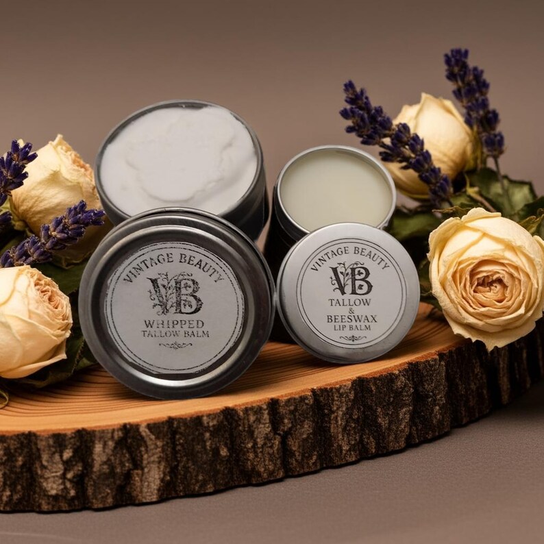 Puede incluir: Una variedad de productos para el cuidado de la piel Vintage Beauty, que incluyen b&aacute;lsamo de sebo batido y b&aacute;lsamo labial de sebo y cera de abejas, en peque&ntilde;os recipientes met&aacute;licos. Los recipientes est&aacute;n dispuestos sobre una tabla de madera con rosas secas y ramitas de lavanda. Las etiquetas muestran el texto "Vintage Beauty".