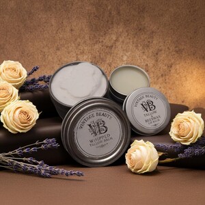 Puede incluir: Una variedad de productos para el cuidado de la piel Vintage Beauty, incluyendo b&aacute;lsamo de sebo batido y b&aacute;lsamo labial de cera de abejas, en peque&ntilde;os botes plateados. Los productos se presentan con rosas crema y ramitas de lavanda.