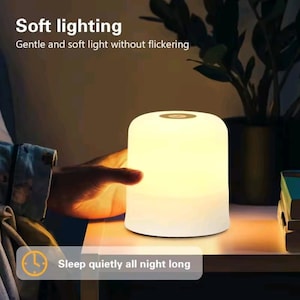 Peut inclure: Lampe de chevet cylindrique et lumineuse avec un dessus arrondi. La lampe émet une lumière douce et chaude, avec le texte "Soft lighting" et "Sleep quietly all night long" visible. La lampe est sur une surface en bois.