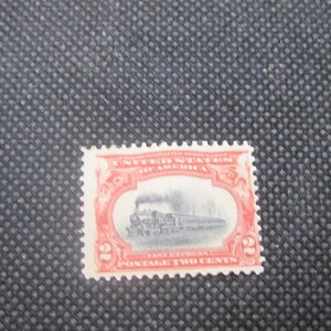 Puede incluir: Un sello postal vintage de los Estados Unidos. El sello, de forma rectangular, presenta un marco rojo y una imagen en blanco y negro de un tren. El texto "Postage Two Cents" es visible. El sello tiene un borde dentado.