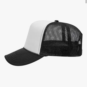 May include: A black and white trucker hat with a mesh back and a curved brim. The front panel is white, and the brim is black. A black rope detail separates the front panel from the brim.