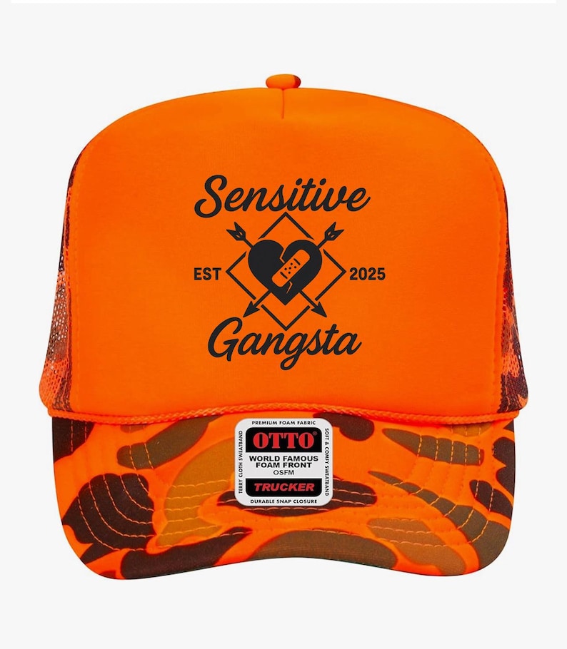 May include: Orange trucker hat with a camouflage pattern on the brim and mesh back. The front features the text "Sensitive Gangsta" with a heart and arrow design. Includes a "World Famous Foam Front" label.