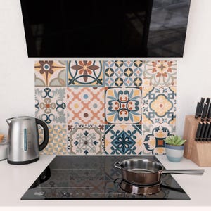 May include: A kitchen scene featuring a decorative backsplash composed of patterned tiles in various colors. A stainless steel kettle and a saucepan are on a black stovetop. A small potted plant and a knife block are also visible.