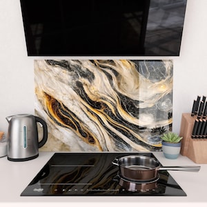 Könnte beinhalten: Eine moderne Küche mit einem schwarzen Induktionskochfeld und einem Edelstahl-Kochtopf. Eine dekorative Rückwand mit Marmoreffekt in Schwarz, Weiß und Gold ist zu sehen. Ein Edelstahlkessel und ein Messerblock aus Holz sind ebenfalls vorhanden.