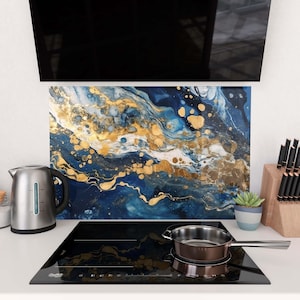 May include: A modern kitchen scene featuring a black stovetop with a stainless steel saucepan. A decorative backsplash with blue and gold abstract art is visible. A stainless steel electric kettle and a small potted succulent are also present.