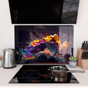 Puede incluir: Una cocina moderna con una placa de cocina negra, una tetera de acero inoxidable y un salpicadero de arte abstracto colorido. El arte presenta vibrantes salpicaduras de amarillo, morado y azul. Una pequeña sartén está en la placa.