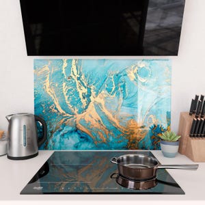 May include: A kitchen backsplash with a blue and gold abstract design. A stainless steel kettle and a small potted succulent are visible. A black cooktop with a stainless steel pan is in the foreground.