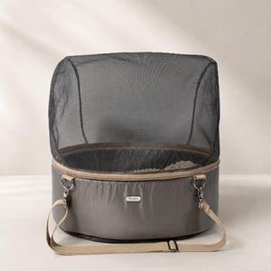 May include: A gray pet carrier with a mesh top and a tan shoulder strap. The carrier has a zippered closure and a small logo on the side. The interior appears to be lined with a soft, light-colored material.