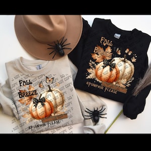 Puede incluir: Dos sudaderas con gráficos de temática otoñal. Una es negra, la otra beige. Ambas presentan un diseño de calabaza con el texto "Fall Breeze & Pumpkin Please". Un sombrero marrón con una araña negra y una araña negra también están en la imagen.
