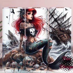 May include: A tumbler with a mermaid design. The mermaid has red hair, tattoos, and a skull-themed top, sitting on a rock. A pirate ship is in the background. The design includes skulls and seashells. The words "Free Designs" are visible.