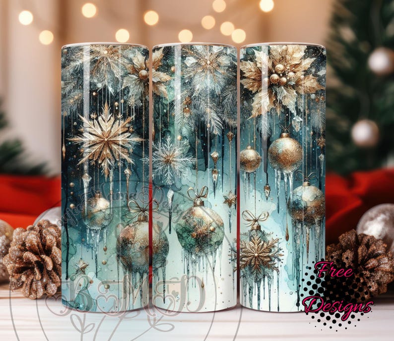 May include: Three cylindrical tumblers with a winter holiday theme. The design features gold and silver snowflakes, ornaments, and dripping icicles against a teal and white watercolor background. The tumblers have the text "Free Designs".