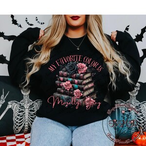 May include: Black long-sleeved sweatshirt with the text "MY FAVORITE COLOR IS Morally Grey". The graphic features a stack of books with pink and black roses. The design includes a floral and book theme.