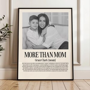 May include: Black and white framed print featuring a mother and child. The text "MORE THAN MOM" is displayed above the name "Grace Clark [noun]" and a description of a mother's role. A decorative piece for the home.
