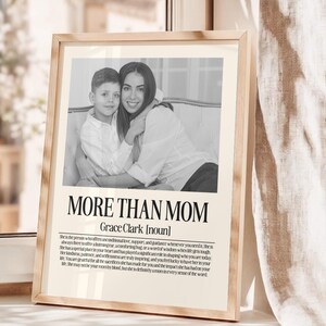 May include: A framed black and white print featuring a photograph of a mother and child. The text "MORE THAN MOM" is displayed prominently, with the name "Grace Clark" below. The print includes a definition of "mom".