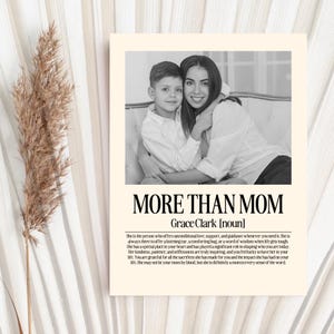 May include: A black and white print with the text "MORE THAN MOM" and a photo of a woman and child. The print includes a definition of the word "mom". The print is on a cream-colored background.