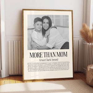 May include: A framed black and white print featuring a mother and child. The text "MORE THAN MOM" is displayed below the image, with additional text describing a mother's role. The frame is a warm, natural wood tone.