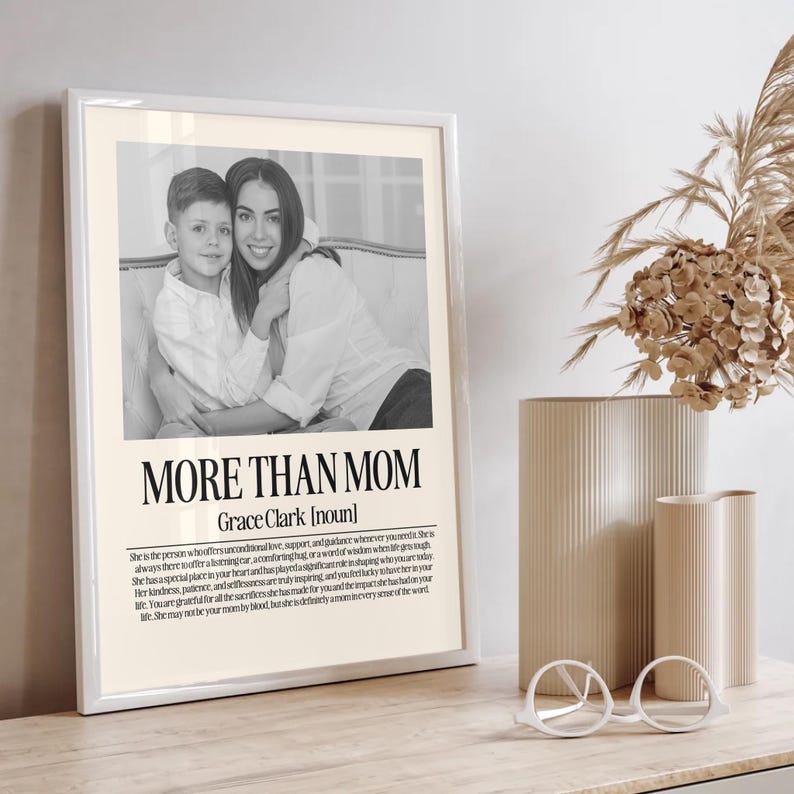 May include: Framed black and white print with the text "MORE THAN MOM" and a definition. The image features a mother and child. The frame is white, and the background is a neutral color.