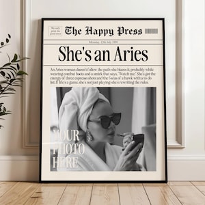 Peut inclure: Impression encadrée avec un design de journal, avec le titre "She's an Aries". L'image montre une femme se maquillant, avec le texte "Your Photo Here". L'impression comprend également le texte "The Happy Press".