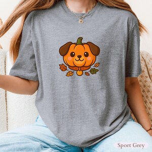 May include: Sport Grey t-shirt with a cartoon dog design. The dog has a pumpkin head, brown ears, and a collar, with autumn leaves around it. The text "Sport Grey" is at the bottom right of the shirt.