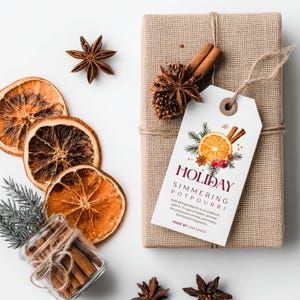 May include: A gift wrapped in burlap with a tag that reads "Holiday Simmering Potpourri." The image includes dried orange slices, star anise, cinnamon sticks, and a small glass jar filled with cinnamon sticks.
