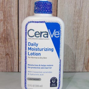 May include: A white CeraVe Daily Moisturizing Lotion bottle with a blue and white label. The bottle is decorated with blue rhinestones around the label and pump. The label includes the text "Daily Moisturizing Lotion" and "12 FL OZ (355 ml)".