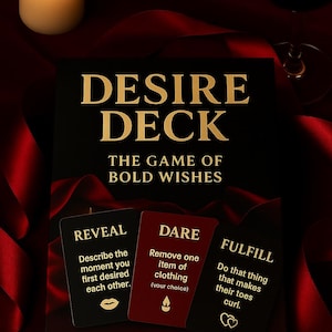 Op de afbeelding: Een zwarte doos met gouden letters met de tekst "DESIRE DECK" en "THE GAME OF BOLD WISHES". Drie kaarten lezen "REVEAL", "DARE" en "FULFILL". Een brandende kaars en een wijnglas staan op de achtergrond.
