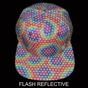 Peut inclure: Casquette de baseball colorée avec un motif géométrique aux couleurs de l'arc-en-ciel. La casquette a une visière plate et le texte "FLASH REFLECTIVE" en bas. Le motif est composé de lignes et de triangles blancs.
