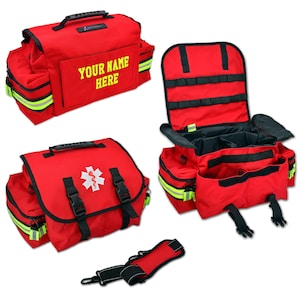 Puede incluir: Bolsa médica de emergencia roja con múltiples compartimentos y un asa. La bolsa presenta rayas reflectantes, hebillas negras y el texto "YOUR NAME HERE" en amarillo. Un símbolo médico es visible.