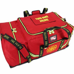Può includere: Una borsa da viaggio rossa con dettagli neri e la scritta "FIRE FIGHTER" sulle cinghie. La borsa ha una cerniera e finiture gialle, con la scritta "YOUR NAME HERE" sulla parte superiore. È visibile un emblema dei vigili del fuoco.