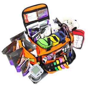 Könnte beinhalten: Eine offene orangefarbene medizinische Tasche, gefüllt mit verschiedenen medizinischen Materialien. Die Tasche enthält mehrere Fächer und Beutel, darunter kleine farbige Beutel, medizinische Instrumente und Pakete mit der Aufschrift "MED POD". Ein Blutdruckmessgerät ist sichtbar.