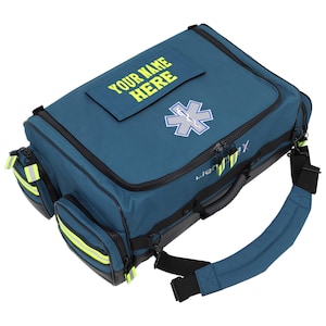 Puede incluir: Bolsa médica de color turquesa con ribete negro, un emblema blanco y azul de la Estrella de la Vida y el texto "YOUR NAME HERE" en amarillo. Cuenta con múltiples compartimentos con cremallera, rayas amarillas reflectantes y una correa acolchada para el hombro.