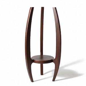 May include: A dark brown wooden plant stand with a round shelf and three legs. The stand has a curved design with two outer supports and a central support, creating a modern aesthetic.