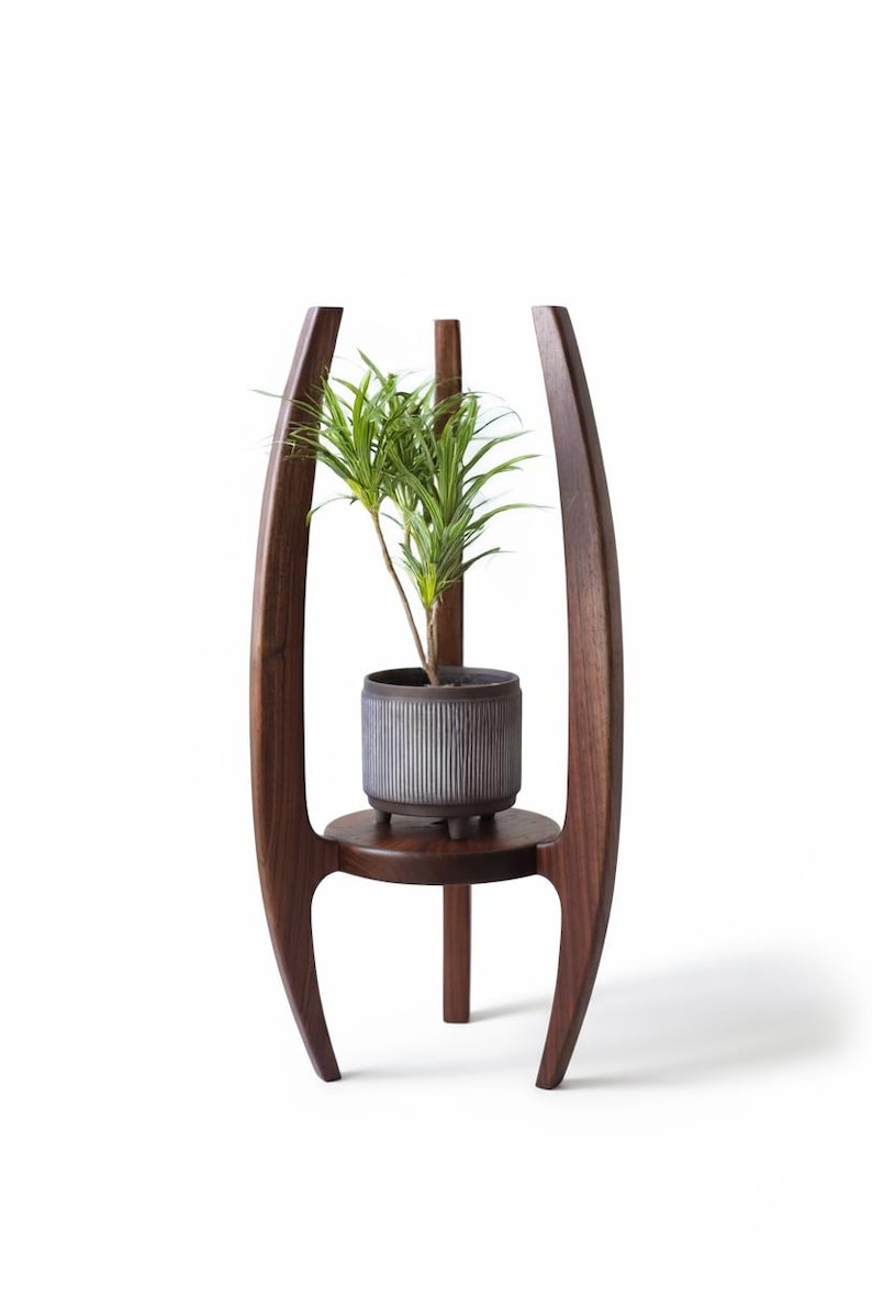 May include: A dark brown wooden plant stand with a modern design. The stand features a circular shelf and a tall, vertical support. A gray, ribbed ceramic pot with a green plant sits on the shelf.