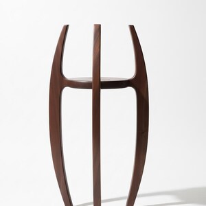 May include: A dark brown wooden side table with a unique, open design. The table features curved legs that rise to meet a circular shelf, with a central vertical support. The overall height is approximately 30 inches.