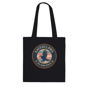 Pode incluir: Uma sacola preta com um gráfico circular apresentando uma ilustração de uma águia. O design inclui listras horizontais em azul, rosa e branco, com o texto RAVENCLAWS FOR TRANS RIGHTS impresso em uma borda circular ao redor da águia.
