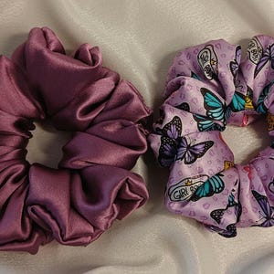 Puede incluir: Dos coleteros. Uno es de color malva liso, el otro es de color lila claro con un estampado de mariposas y las palabras "GIRL BOSS". Estos accesorios para el cabello están hechos de una tela suave y sedosa.
