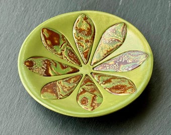 May include: A ceramic dish with a lime green base and eight petal-shaped compartments. The petals are a mix of green, brown, and gold, creating a unique, organic design. The dish is likely used for serving or display.