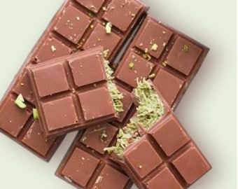 May include: Several chocolate bars with a light brown color are arranged on a light background. Some bars are broken, revealing a green filling. The chocolate bars are square-shaped and have a smooth texture, with small green pieces sprinkled on top.