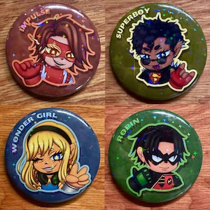 May include: Four circular pin-back buttons featuring holographic star patterns. The top left button is brown with Impulse text and character. The top right is olive green with Superboy text and character. The bottom left is blue with Wonder Girl text and character. The bottom right is green with Robin text and character.